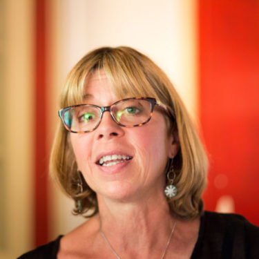 CarolineMediumSizePicsTour2-Headshot-e1499876141278-375×375 a woman wearing glasses and smiling at the camera